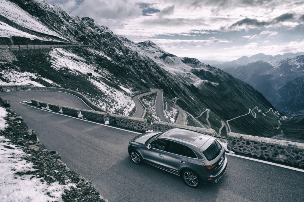 A luxury car twists and turns down a highway along a snowy mountain side. 