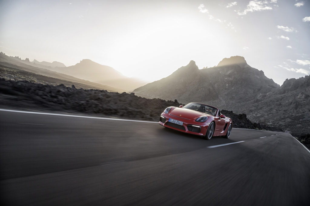 A red luxury car speeds down a highway. 