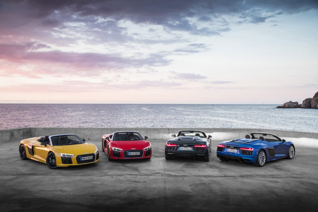 Four luxury cars of different colors are parked by the ocean. 