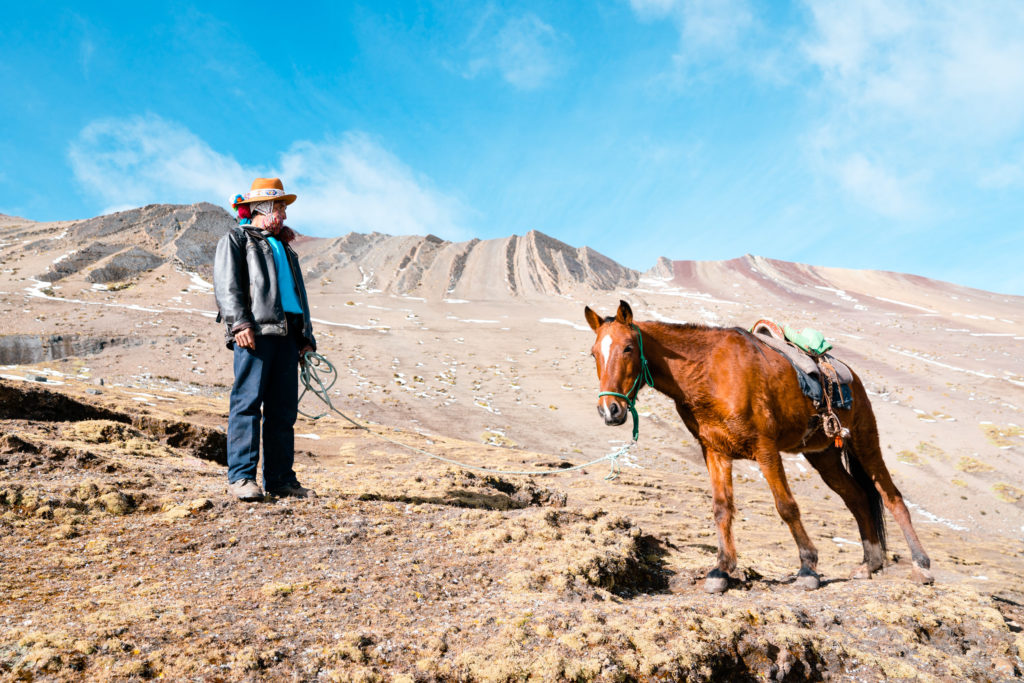 A sherpa walks a horse through cold dry land. 