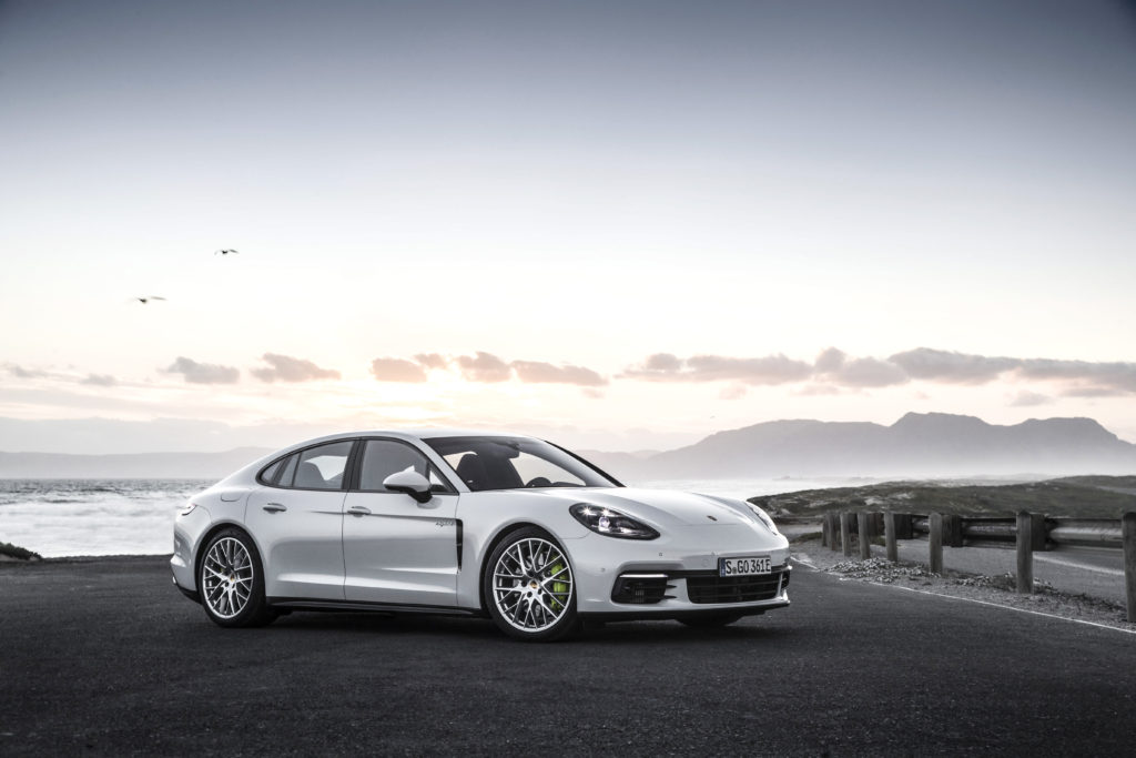 A white luxury car is parked by the ocean on the side of the road. 