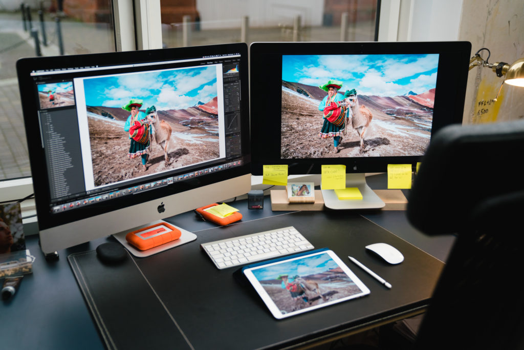 A desk with two monitors and a tablet all with a photo of a woman walking a lama. 