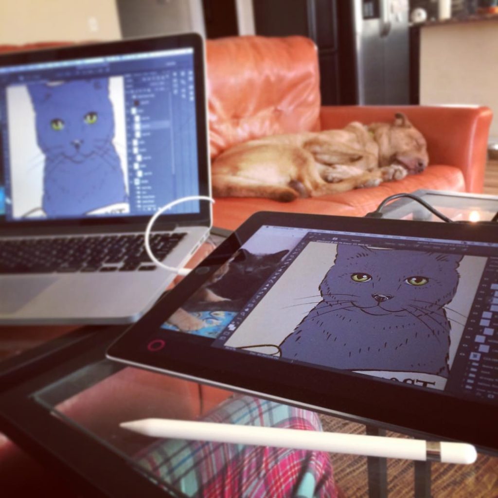 A designer works on digitally drawing a cat on a tablet while also using a computer. 