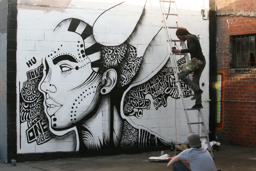 An artists paints a black and white female face on the side of a building. 