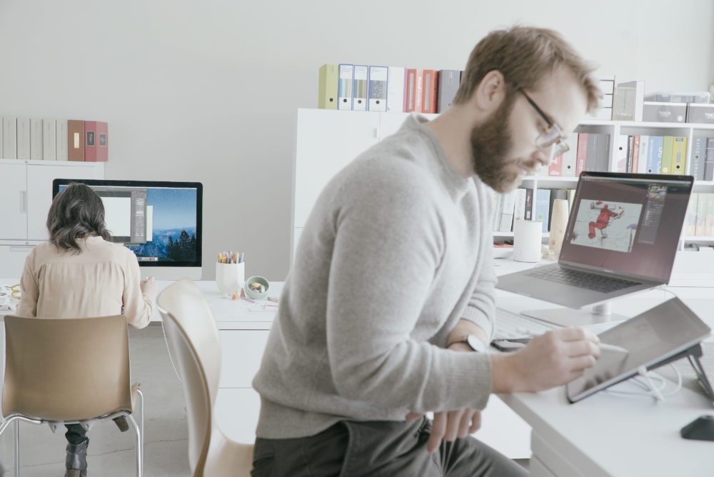 Two people work on tablets in a modern and bright white office. 