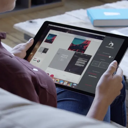 A woman sits on a couch holding an iPad with a presentation on it