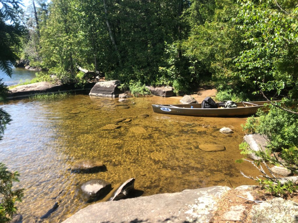 A canoe sits on the banks of a clear water river. 