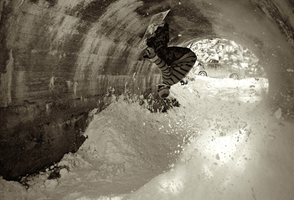 A snowboarder rides the top of a tunnel. 