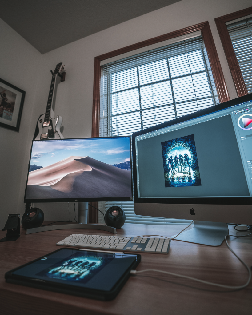 Jeff Kepler's work space includes two monitors, a tablet, and a guitar hanging on the wall. 