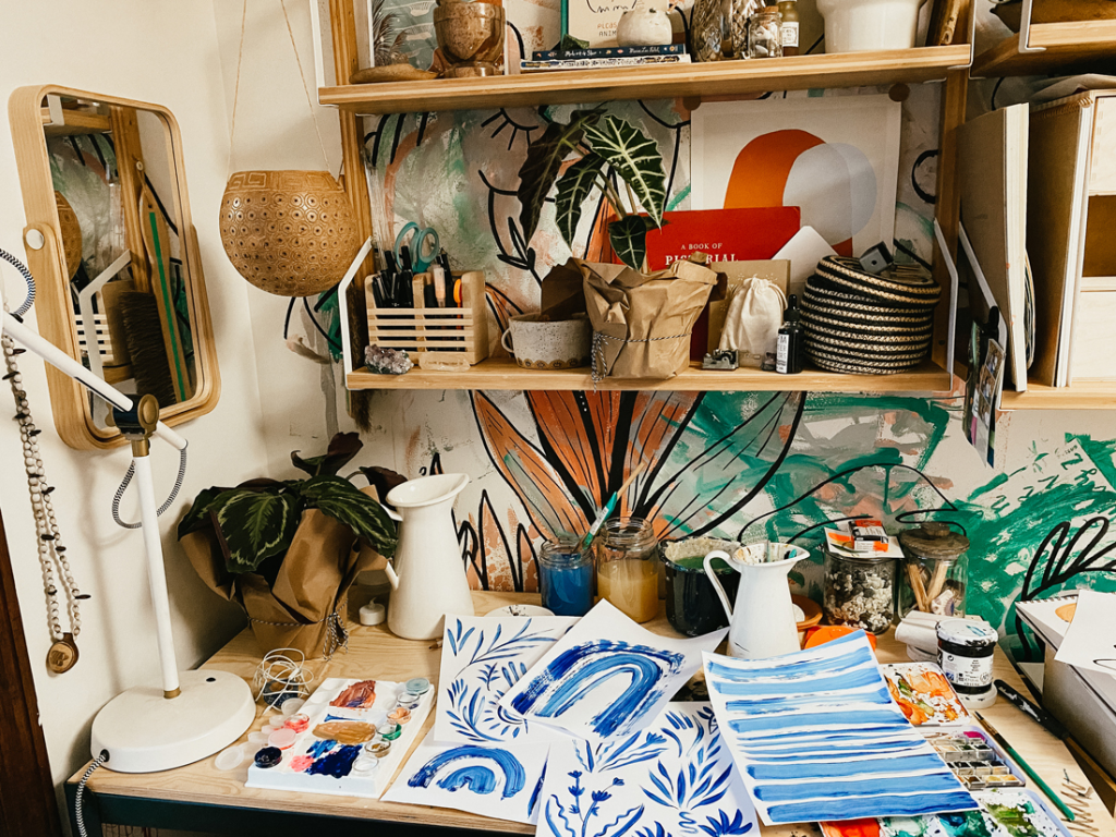 An artists desk full of paintings and art supplies. 