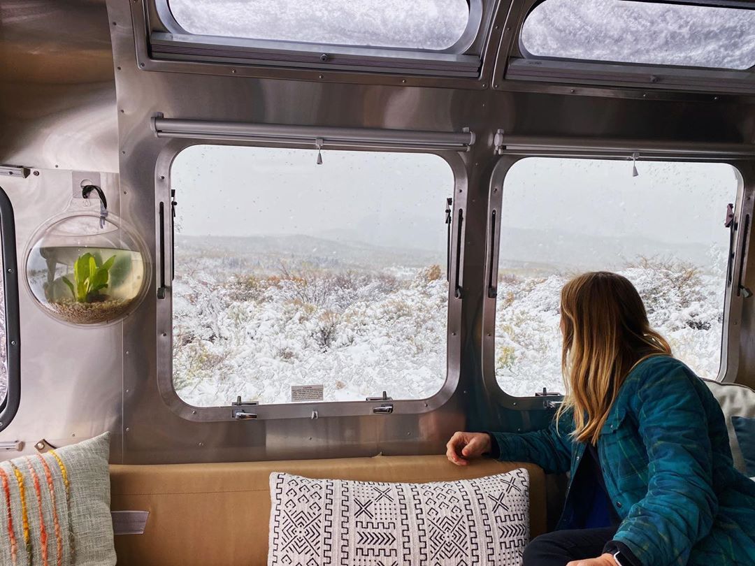 Stacey Powers looks out the window of her camper van overlooking a snowy desert.