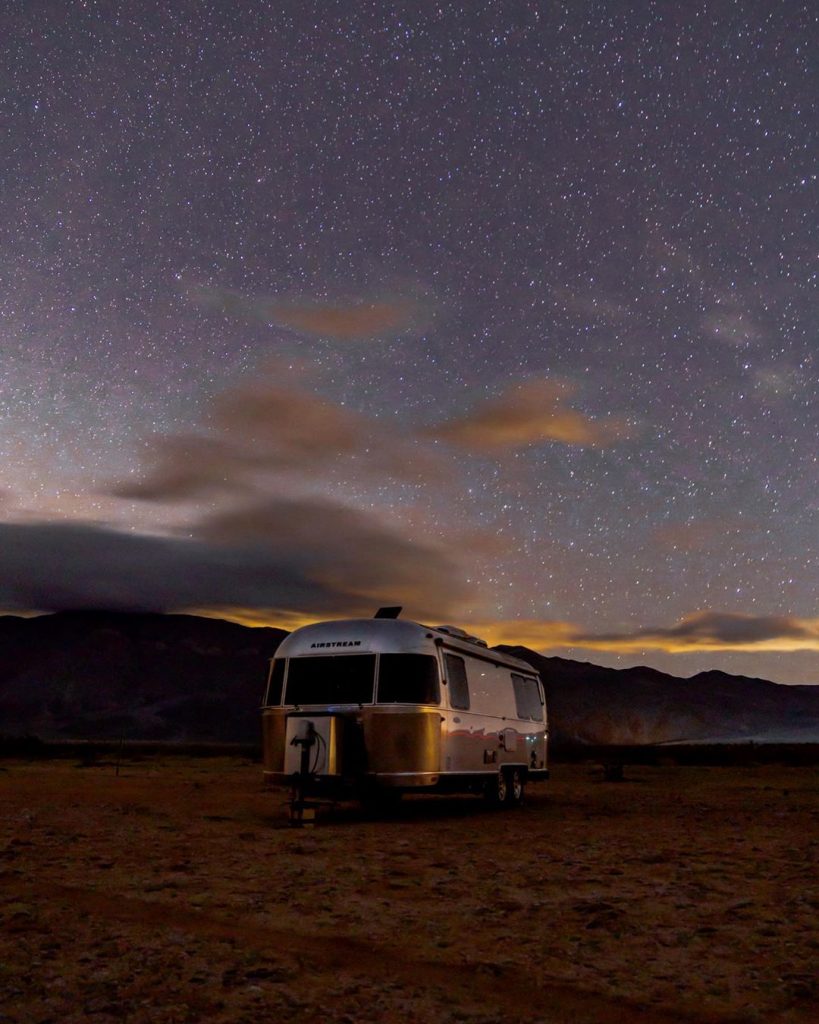 An airstream RV under a star filled night in the desert. 