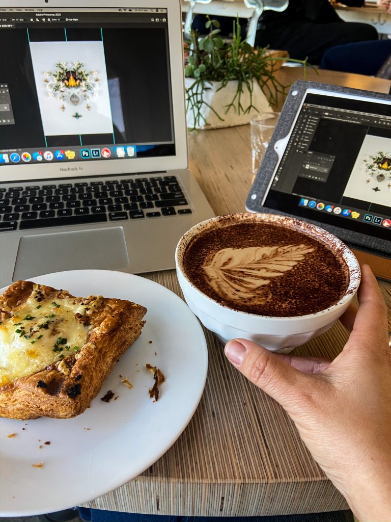 Rachel sitting in a cafe enjoying a sweet treat while working on her laptop and tablet. 