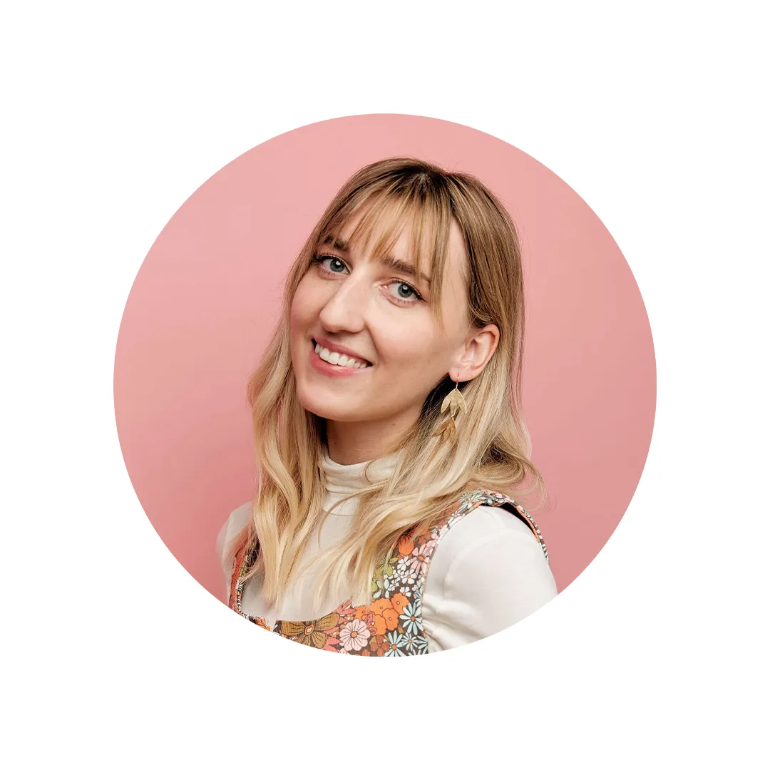 A headshot of a woman smiling at the camera with a pink background