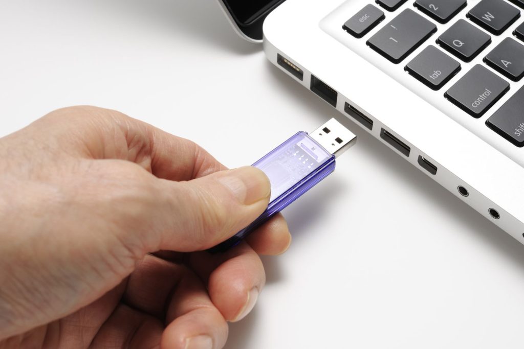 a hand plugging a flash drive into a computer 