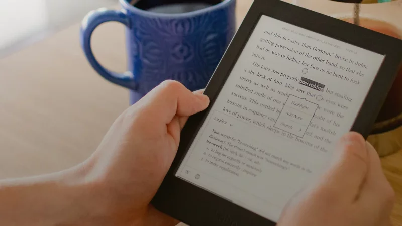 hands holding a kobo e-reader next to a cup of coffee