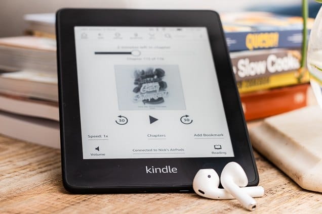 Kindle with an audiobook pulled up on the screen and airpods resting next to the kindle. 