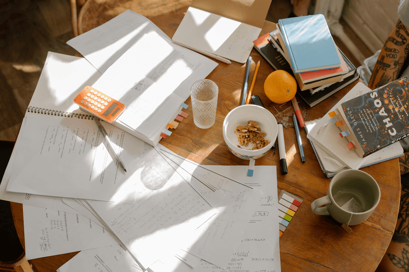 A table littered with note-taking supplies, books, notes, and snacks