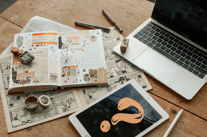 An iPad with a question mark on it next to a notebook of warm aesthetic notes and a laptop. Note-taking supplies surround these items.